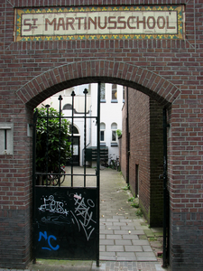 819063 Gezicht door de toegangspoort van de voormalige St.-Martinusschool (Oudegracht 395 - 397) te Utrecht.